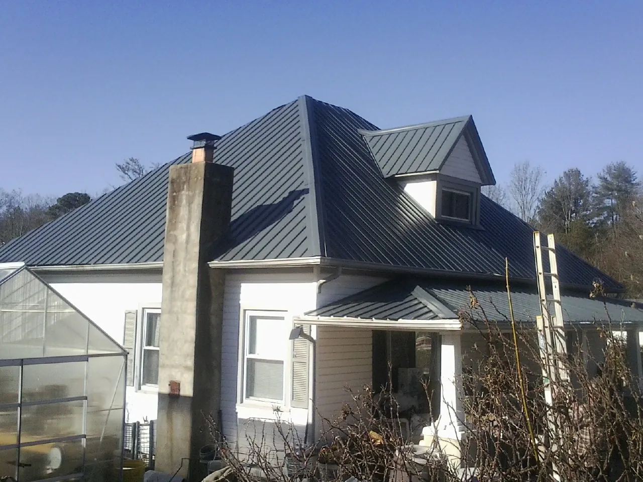 Dark blue standing seam metal roof on a white farmhouse with dormer — Slate & Tile Roof Repair by Roofing Brothers in Maywood
