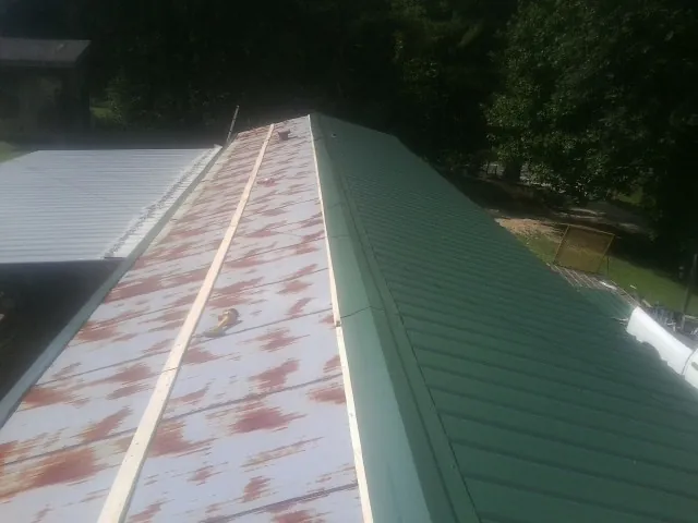 Old rusted panels beside newly installed green metal roofing — Wind Damage Roof Repair by Roofing Brothers in Maywood
