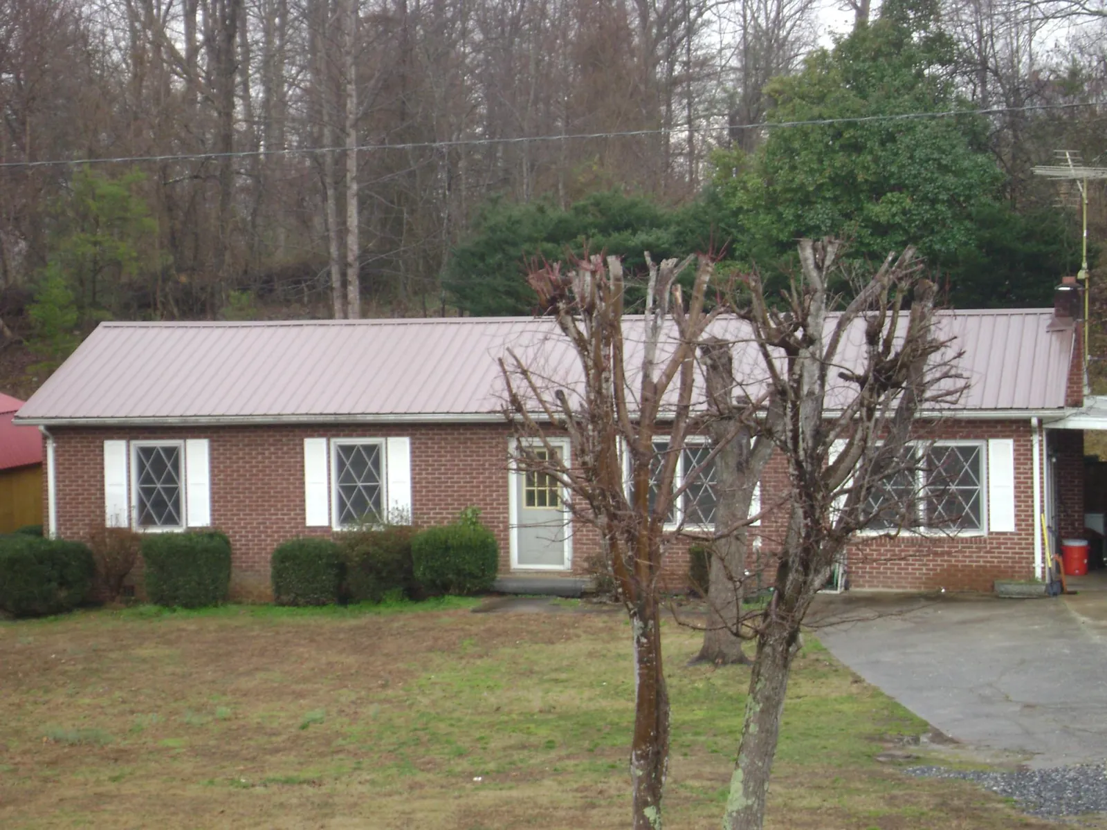 Mauve metal roof on a brick ranch home behind bare trees in Maywood